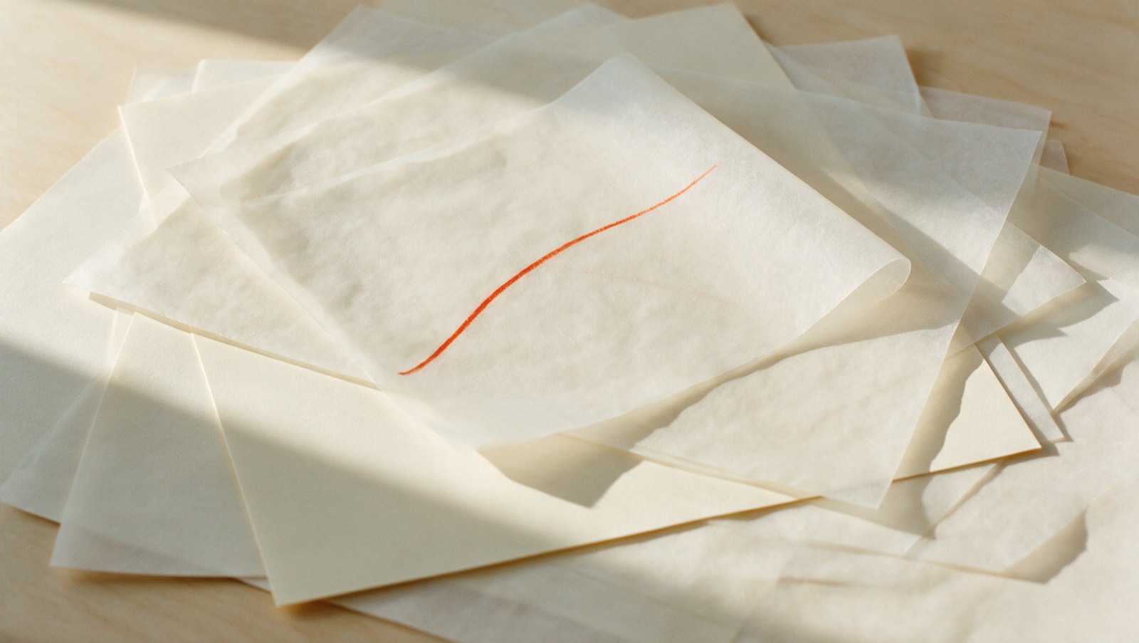 Overlapping sheets of vellum on a cream desk, one marked in red