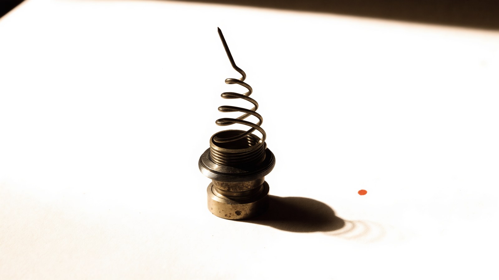 A brass helical antenna coil standing on warm paper in raking light